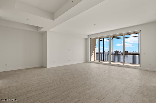 unfurnished room with light wood-style floors, a water view, a raised ceiling, and baseboards