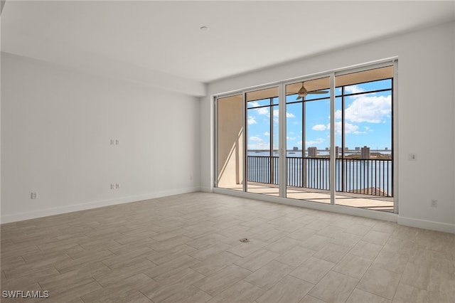 unfurnished room with light wood-type flooring, a water view, and baseboards