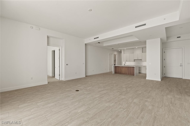 unfurnished living room with baseboards, visible vents, light wood-style flooring, and a sink