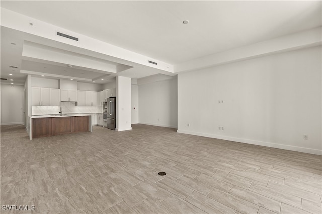 unfurnished living room with a tray ceiling, visible vents, light wood finished floors, and baseboards