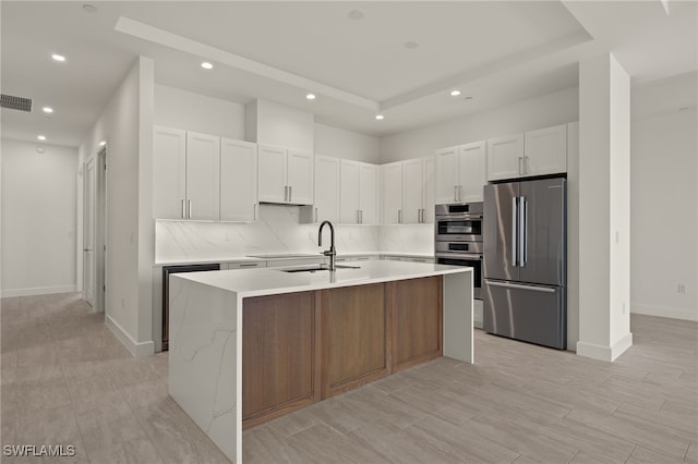 kitchen with light countertops, visible vents, appliances with stainless steel finishes, a kitchen island with sink, and a sink