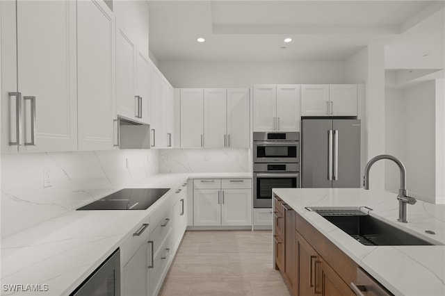 kitchen featuring tasteful backsplash, light stone countertops, stainless steel appliances, white cabinetry, and a sink