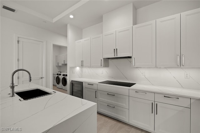 kitchen featuring wine cooler, black electric stovetop, washing machine and clothes dryer, visible vents, and a sink