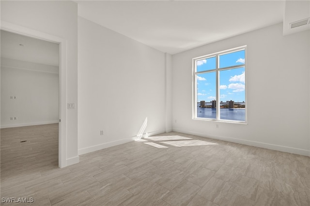 empty room with light wood-style floors, visible vents, and baseboards