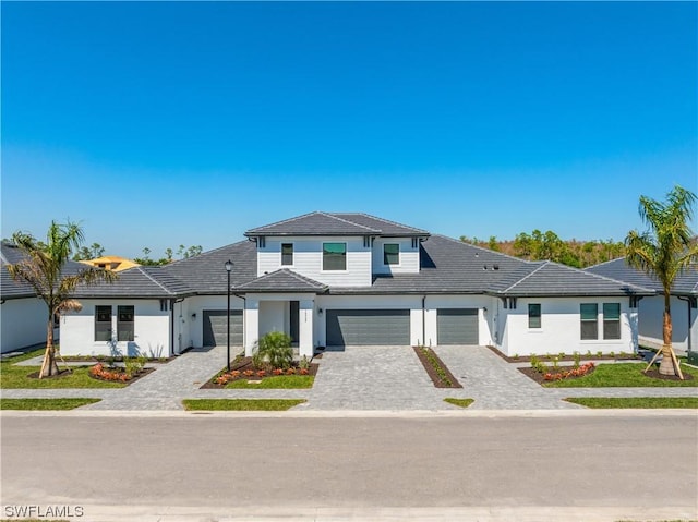 view of front facade featuring a tiled roof, decorative driveway, an attached garage, and stucco siding