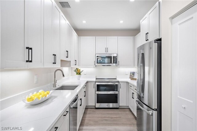 kitchen featuring white cabinetry, sink, light stone counters, appliances with stainless steel finishes, and light wood-type flooring