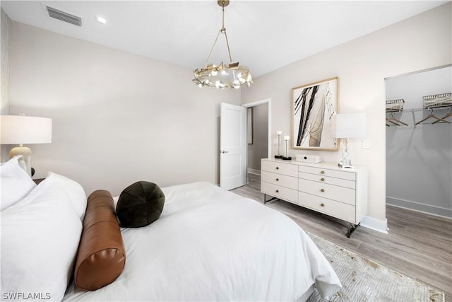 bedroom with a spacious closet, a notable chandelier, wood-type flooring, and a closet