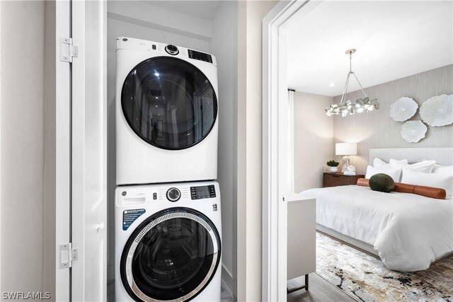 clothes washing area with hardwood / wood-style floors, an inviting chandelier, and stacked washer / dryer