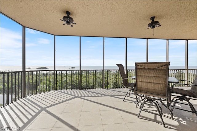 sunroom with plenty of natural light, ceiling fan, and a water view