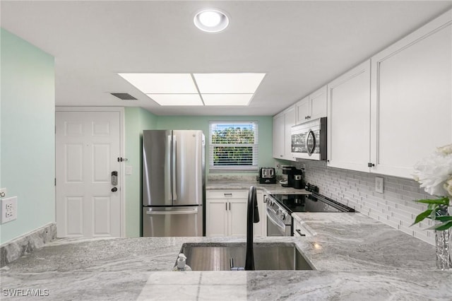 kitchen featuring appliances with stainless steel finishes, tasteful backsplash, light stone counters, sink, and white cabinets