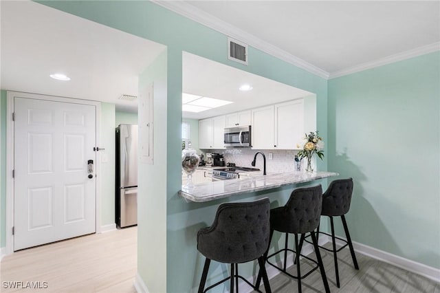 kitchen featuring white cabinetry, light stone counters, kitchen peninsula, appliances with stainless steel finishes, and light wood-type flooring