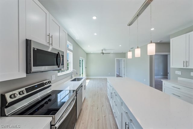 kitchen with stainless steel appliances, hanging light fixtures, sink, white cabinets, and light hardwood / wood-style flooring