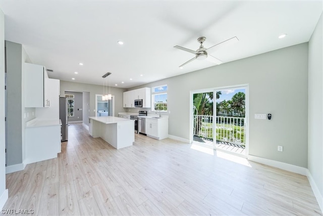 kitchen with stainless steel appliances, a kitchen island, white cabinetry, decorative light fixtures, and light hardwood / wood-style floors