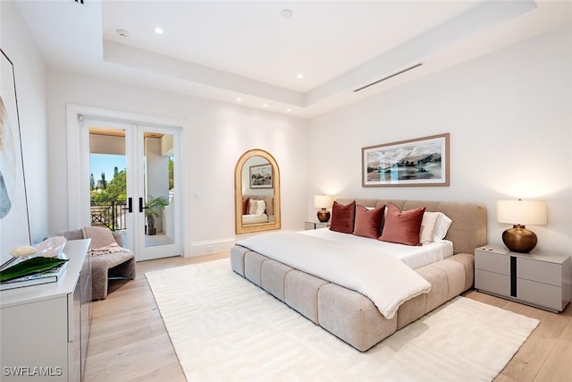 bedroom featuring a tray ceiling, access to outside, french doors, and light wood-style floors