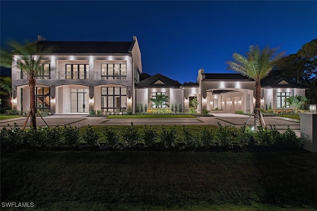 back of house at twilight with a balcony, a yard, and stucco siding