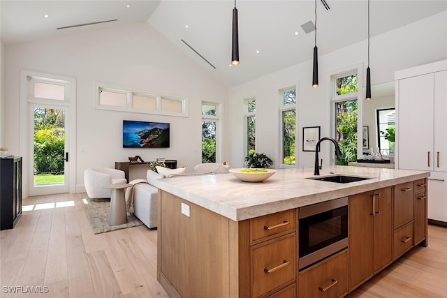 kitchen featuring brown cabinets, light wood-style flooring, a sink, stainless steel microwave, and light countertops