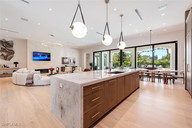 kitchen with light stone counters, a large island with sink, light wood-style flooring, and a sink