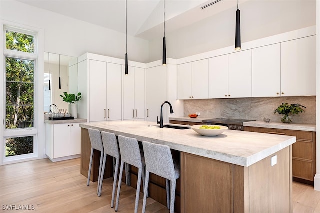 kitchen featuring a center island with sink, light wood-style flooring, a sink, a kitchen bar, and tasteful backsplash