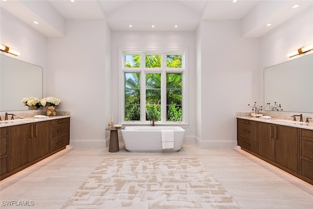 full bath featuring a soaking tub, two vanities, baseboards, and a sink