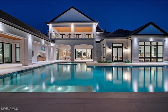 back of house at night with a patio, a balcony, an outdoor kitchen, stucco siding, and french doors