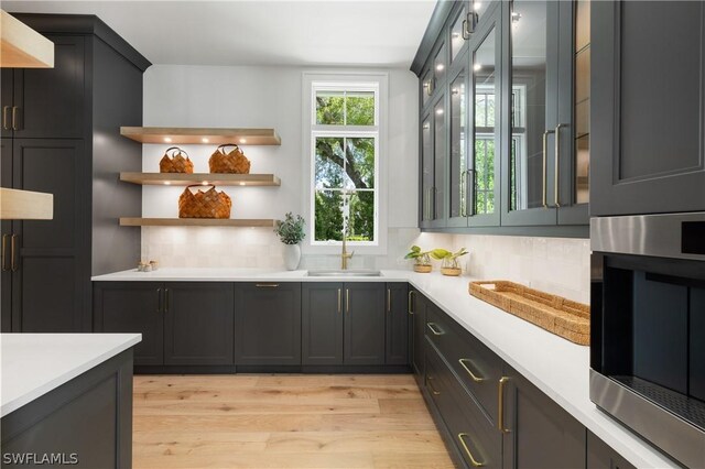 bar with backsplash, sink, stainless steel oven, and light hardwood / wood-style flooring