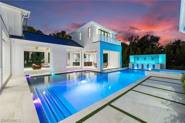 pool at dusk featuring a jacuzzi, an outdoor living space, and a patio area