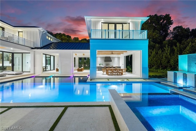 pool at dusk featuring area for grilling, a patio area, and an in ground hot tub