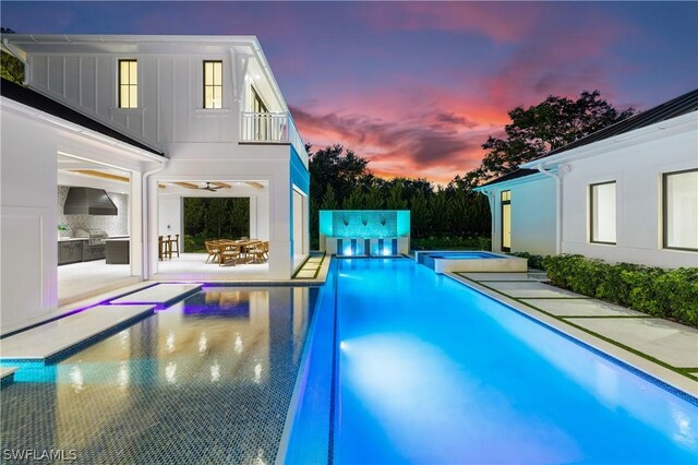 pool at dusk featuring an in ground hot tub, ceiling fan, and an outdoor kitchen