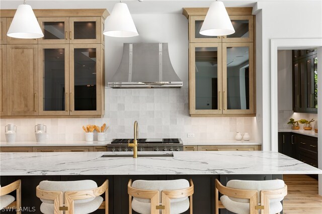 kitchen featuring a kitchen bar, light stone countertops, tasteful backsplash, wall chimney range hood, and decorative light fixtures