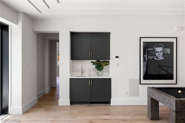 bar with tasteful backsplash, sink, and light wood-type flooring