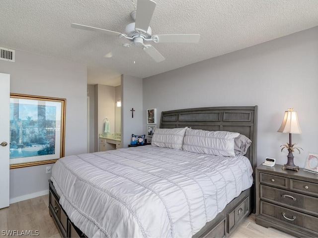 bedroom featuring a textured ceiling, ceiling fan, ensuite bathroom, and light hardwood / wood-style flooring