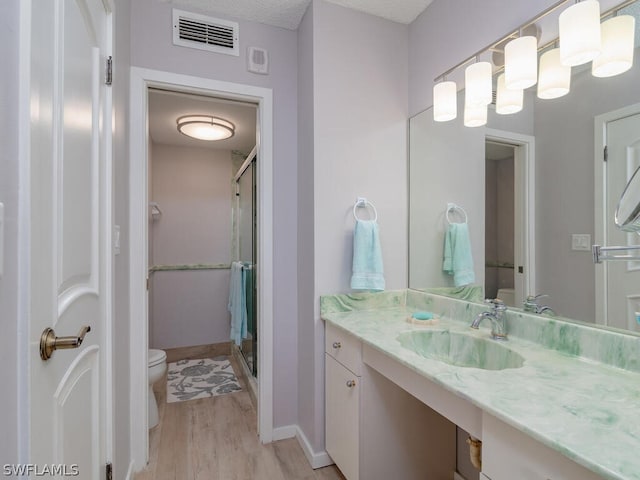 bathroom with toilet, a shower with shower door, hardwood / wood-style flooring, a textured ceiling, and vanity