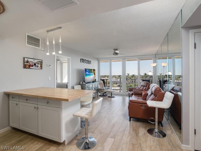 living room featuring light hardwood / wood-style flooring, ceiling fan, a textured ceiling, and a wall of windows