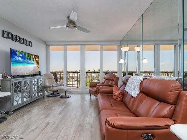 living room with a wall of windows, ceiling fan, light hardwood / wood-style flooring, and a textured ceiling