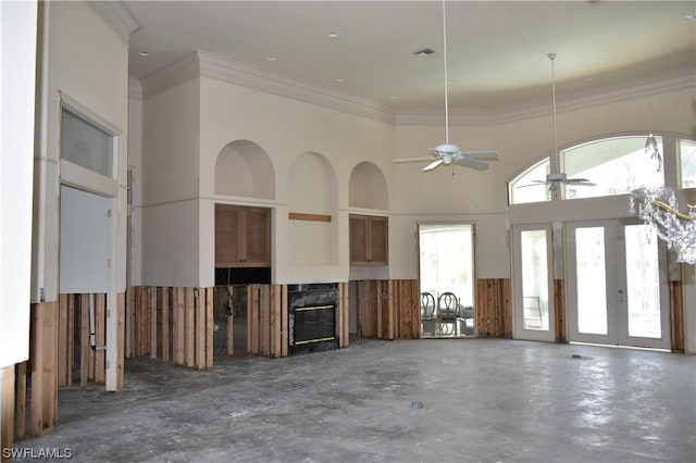 unfurnished living room featuring crown molding, a towering ceiling, a premium fireplace, and ceiling fan