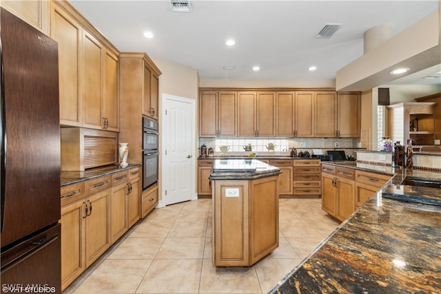 kitchen featuring black refrigerator, backsplash, light tile floors, dark stone counters, and a kitchen island