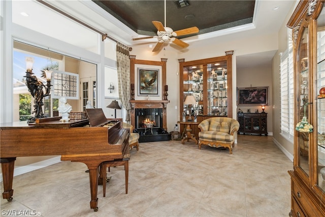 living area with ceiling fan, a raised ceiling, and light tile flooring