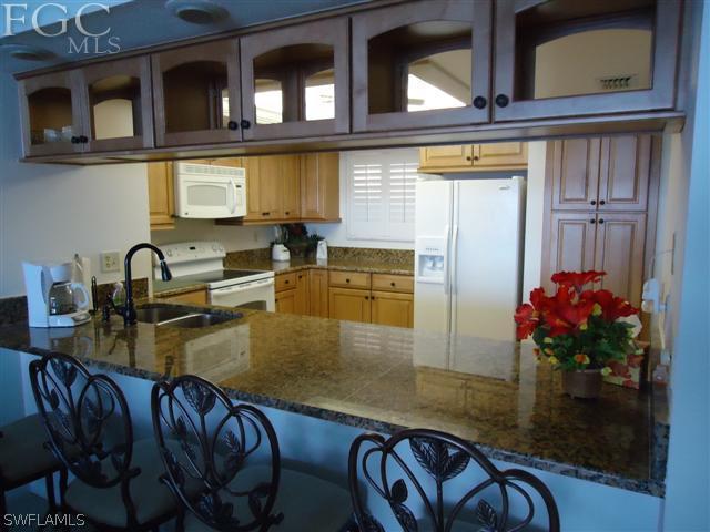 kitchen with white appliances, dark stone counters, a breakfast bar area, and sink