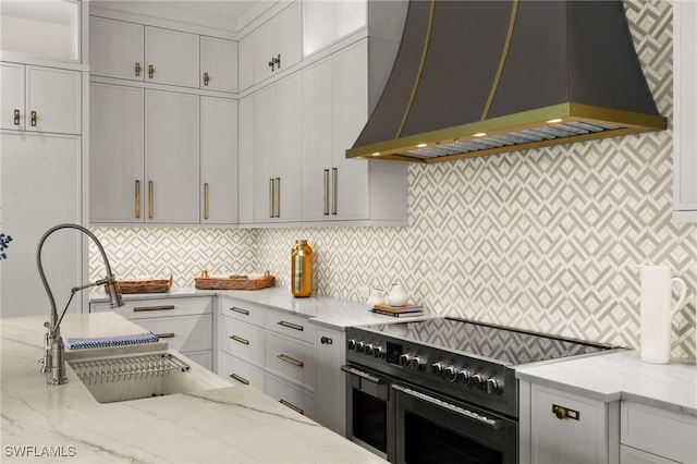 kitchen featuring custom exhaust hood, range with two ovens, light stone counters, and tasteful backsplash