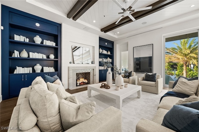 living room with hardwood / wood-style floors, built in shelves, ceiling fan, a premium fireplace, and beamed ceiling