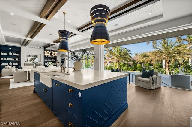 kitchen featuring beam ceiling, sink, a kitchen island with sink, and dark wood-type flooring