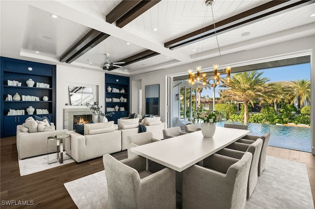 dining area featuring beam ceiling, built in shelves, dark hardwood / wood-style flooring, and ceiling fan with notable chandelier