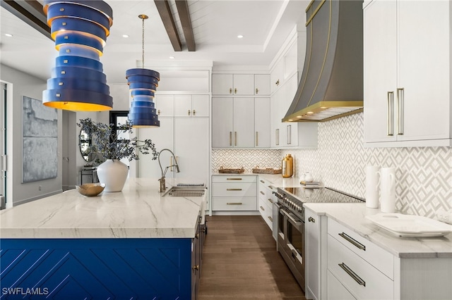 kitchen with a kitchen island with sink, white cabinetry, double oven range, and wall chimney range hood