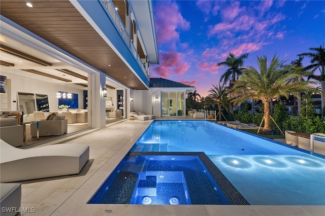 pool at dusk featuring an in ground hot tub and a patio