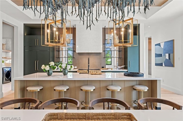 kitchen featuring light wood-type flooring, a breakfast bar, an inviting chandelier, washer / dryer, and built in fridge