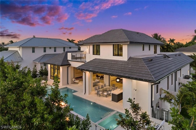 back house at dusk featuring a balcony and a patio