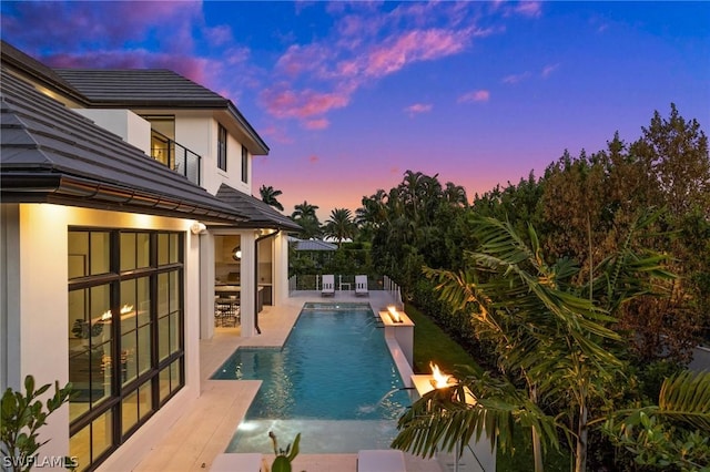 pool at dusk featuring pool water feature, a patio, and an outdoor fire pit