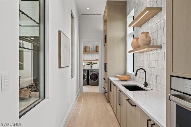 kitchen featuring wall oven, backsplash, light stone counters, sink, and washing machine and clothes dryer