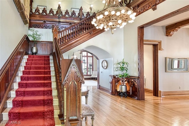 stairs with a towering ceiling, wood-type flooring, beam ceiling, and a notable chandelier