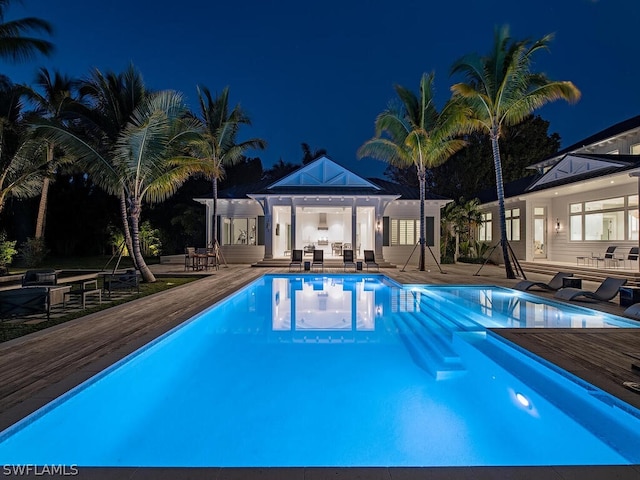 pool at night with outdoor lounge area, a patio, and a deck